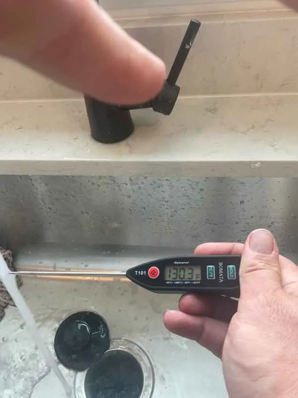 Probe thermometer reading 130.3 degrees Fahrenheit in the hot water stream at a kitchen sink in a new construction home