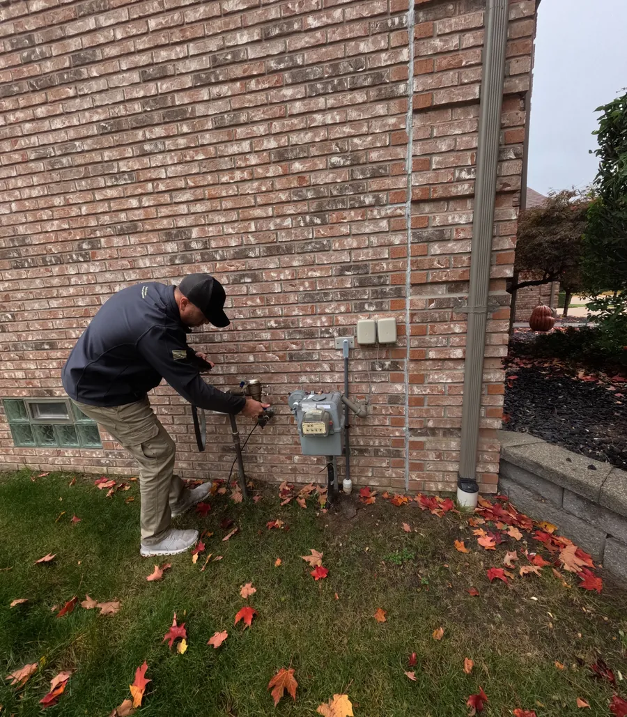 Home inspector checking an irrigation backflow valve on the side of a brick house