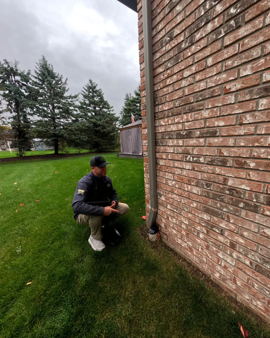 Home inspector checking where a downspout discharges next to a brick foundation